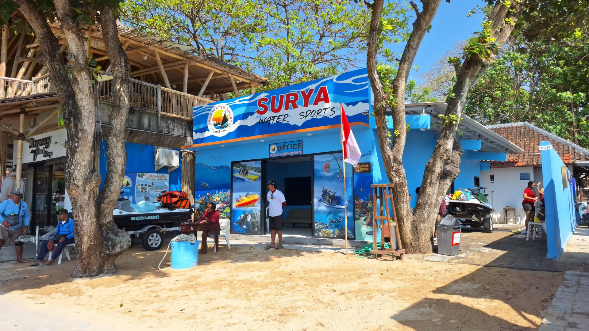The main office building of Surya Watersport, a bright blue structure with several jetskis parked outside, in Sanur, Bali