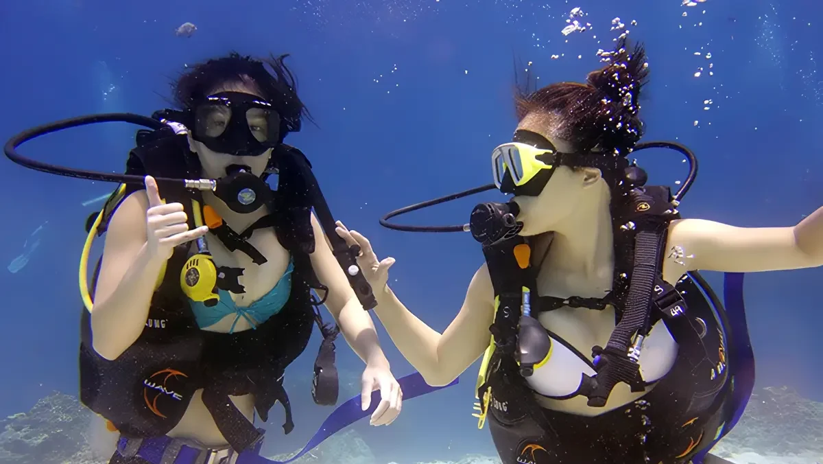 Two female scuba divers exploring a coral reef and giving a thumbs-up gesture in the waters of Sanur, Bali