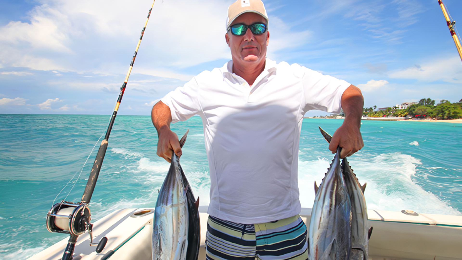 A man on a boat proudly holding up two large tuna fish he caught during a fishing tour in Bali