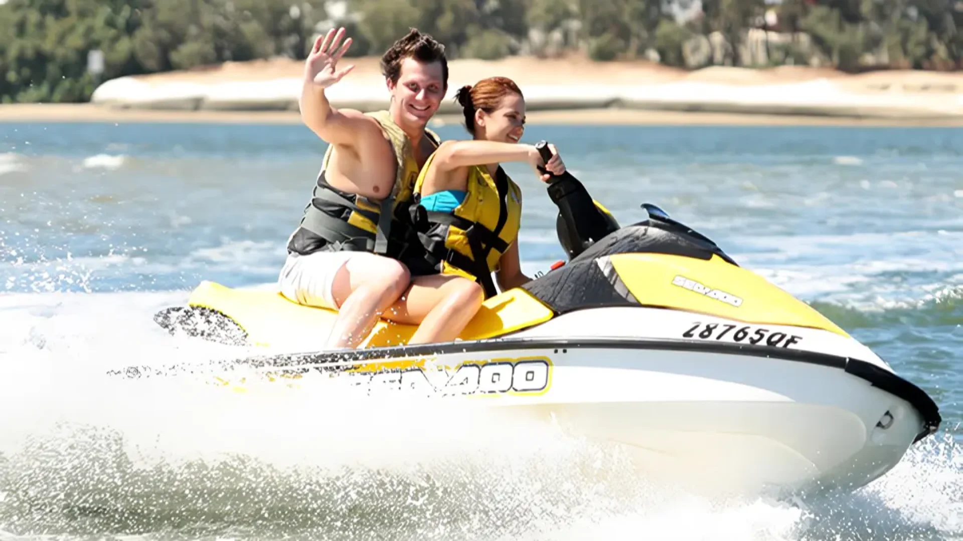 A happy couple riding a jetski and waving at the camera on the water in Sanur, Bali