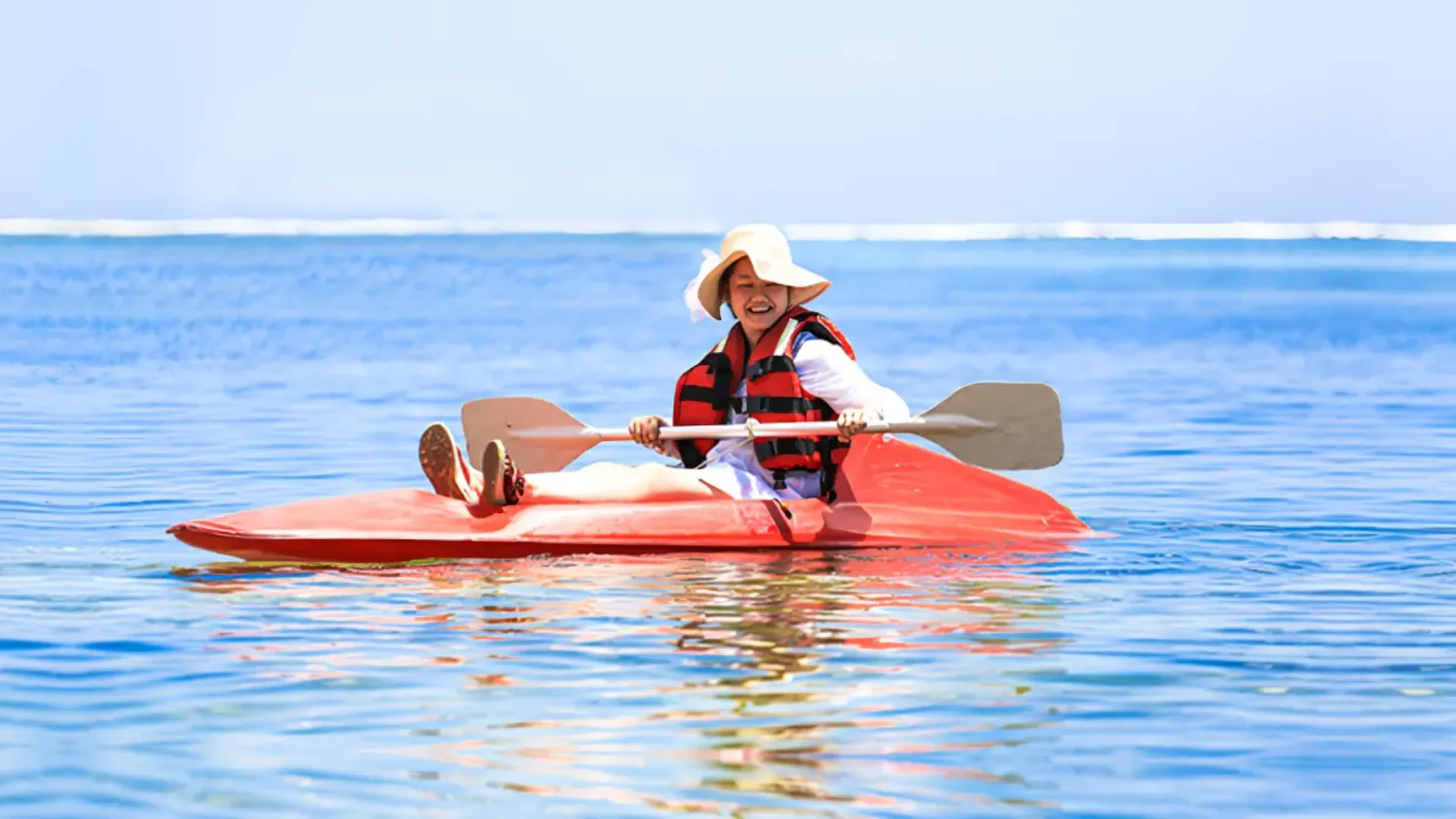 A child in a life jacket smiling while sitting in a red canoe in the calm waters of Sanur, Bali