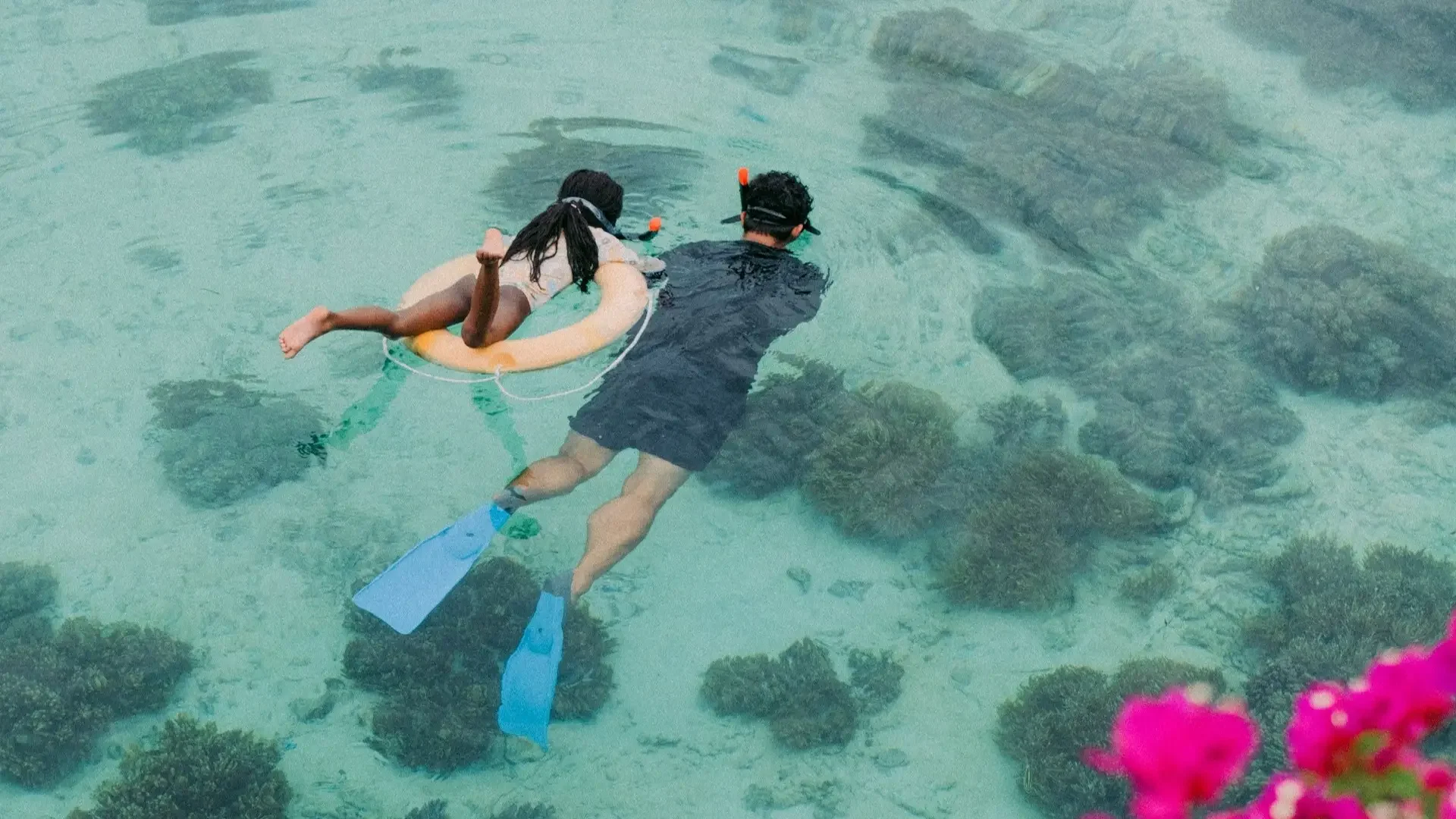 A man and a child snorkeling with a life ring over a coral reef in the clear waters of Sanur, Bali