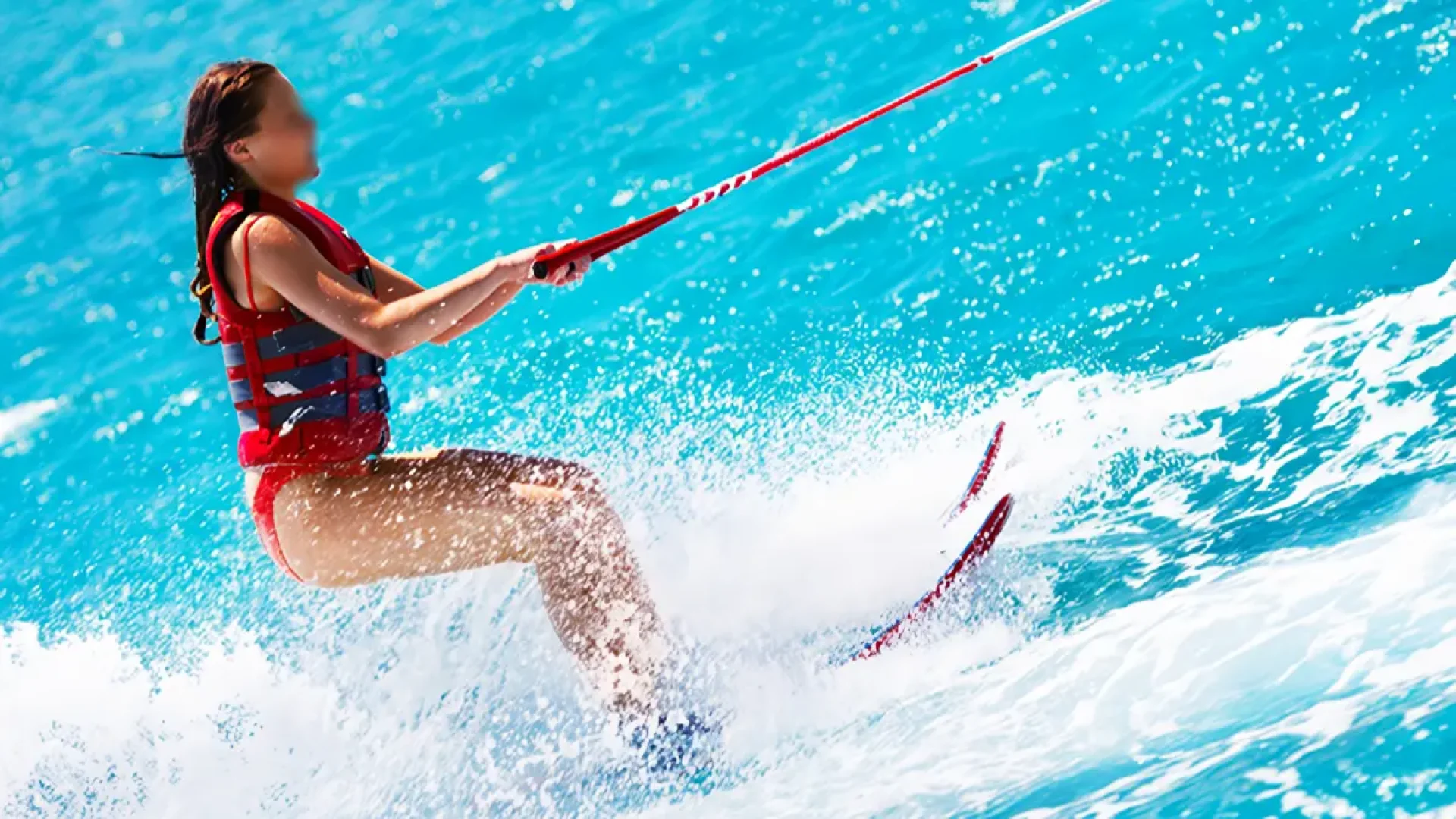 A woman water skiing and holding onto the tow rope, creating a large spray of water in Sanur, Bali